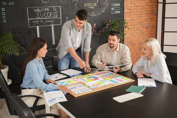 Canvas Print - Young man with his colleagues working on business plan at table in office