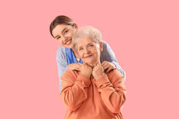 Wall Mural - Nurse hugging senior woman on pink background