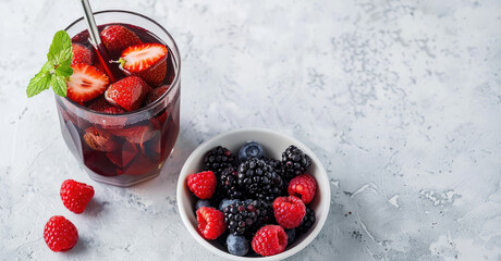 Wall Mural - Refreshing berry drink with fresh strawberries, raspberries, blueberries, and blackberries in bowl on light background