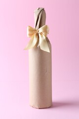 Sticker - Wine bottle in burlap bag with satin bow on pink background