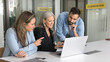 © fizkes - Senior mentor woman training staff of employees, showing professional app, software, online presentation, content on laptop, sitting at workplace. Diverse team working together at computer