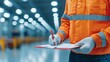 © Jenjira - A safety officer wearing an orange uniform conducts an inspection, taking notes on a clipboard in a well-lit industrial setting.