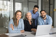 © fizkes - Happy diverse business team posing for professional corporate portrait at workplace. Multiethnic different aged group of colleagues looking at camera with toothy smile, sitting at table with laptop