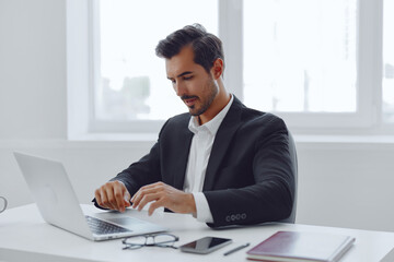 Wall Mural - Man in office businessman sitting at desk and working in laptop and talking on phone, modern suit, finance and startup concept and data analysis, working lifestyle in bright office.