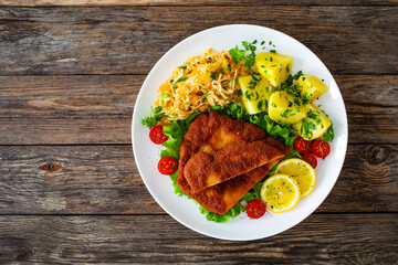 Wall Mural - Crispy breaded fried pork chop, boiled potatoes and sauerkraut salad served on white plate on wooden table
