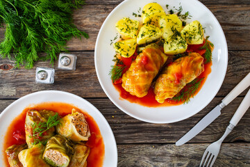 Sticker - Wrapped minced meat in cabbage leaves served in tomato sauce with boiled potatoes on white plate on wooden table - polish dish gołąbki. Top view
