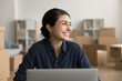 © fizkes - Laughing Indian woman sitting at desk with laptop in warehouse, working on-line, manage orders, create marketing campaign, feel satisfied with sales growth and successful small business development