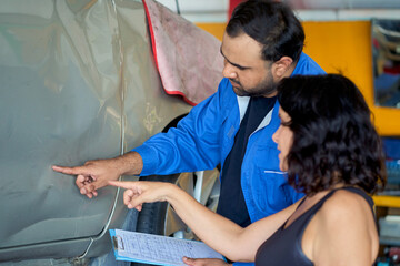 Technician man take a customer to declare car defect from cash accident in car garage.