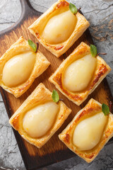 Tasty poached pears are filled with nuts and baked on top of puff pastry closeup on the wooden board on the table. Vertical top view from above