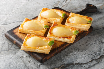 Pears poached in sweet vanilla cinnamon liquid and baked in puff pastry closeup on the wooden board on the table. Horizontal