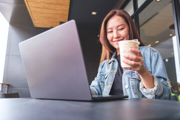 Wall Mural - Portrait image of a young woman drinking coffee while working on laptop computer in cafe