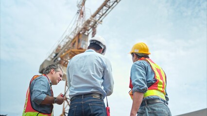 Wall Mural - Group of workers at construction site are discussing construction progress with a tower crane in the background