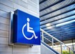 © Wanlop - A sleek, modern wheelchair accessibility sign with bold blue and white graphics, mounted on a wall near a ramp in a contemporary public building.