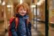 © cochisevisuals - A young boy with red hair smiles while carrying a red backpack in a hallway.