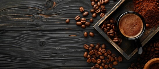 Poster - Top view of ground coffee in a portafilter for espresso set on a wooden tray surrounded by coffee beans against a black wooden background with copy space image