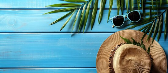 Poster - Image of a palm leaf hat sunglasses on a blue wooden surface with copy space for text evoking a summer and holiday theme