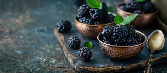 Poster - Fresh blackberries with leaves arranged in vintage copper dishes on rustic wooden boards with a spoon nearby against a dark backdrop in a copy space image
