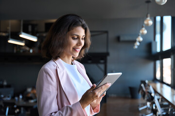 Wall Mural - Young latin Hispanic adult professional business woman looking at online trade app. European mature businesswoman CEO holding digital tablet using fintech tab application working in workspace office