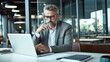 © halo - A middle-aged man in glasses is sitting at a table with his laptop and papers, looking thoughtful while working on an online project for work or home decoration.