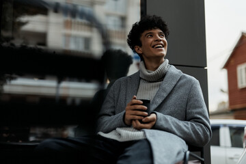 Wall Mural - Young man sitting in chair with coffee, smiling at camera