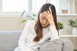 © KMPZZZ - Dizzy asian young woman, girl headache or migraine pain suffering from vertigo while sitting on couch in living room at home, holding head with hand, health problem of brain or inner ear not balance.