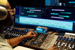 © pressmaster - Man in studio wearing headphones and editing audio tracks on multiple monitors, manipulating a digital audio workstation, surrounded by professional audio equipment and gadgets