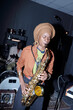 © pressmaster - African American musician playing saxophone at indoor venue with a drummer in background. Musical equipment and instruments surrounding the scene