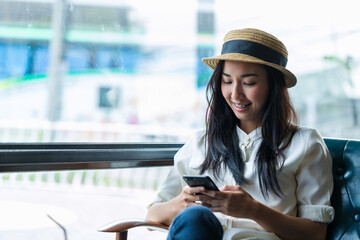 Beautiful Asian businesswoman is smiling and relaxing with texting by smartphone wearing hat in cafe and coffee shop, technology, lifestyle