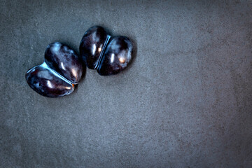 Two purple plums on a dark textured background. Close-up of two dark purple plums lying side by side on a dark textured surface. Top view. Free space for text.