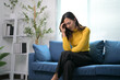 © Parichat - Woman in Yellow Sweater Sitting on Blue Sofa with Headache in Modern Living Room