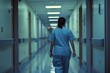© Victor Bertrand - A healthcare worker in scrubs walks down a well-lit hospital corridor, characterized by its sterile and clean environment.