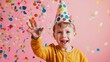 © VK Studio - A smiling young boy in a yellow shirt celebrates as colorful confetti rains down on him, wearing a multicolored polka dot party hat.