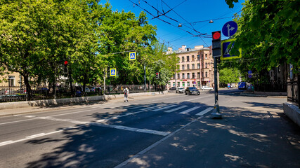 A person crossing an empty city street at a pedestrian crosswalk on a sunny day, highlighting urban safety and summer leisure