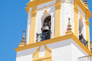 A close-up view of a historic church bell tower in Ronda, Spain, featuring classic yellow and white architectural details against a clear blue sky. Ideal for cultural and architectural themes.