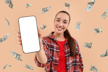 Happy woman showing mobile phone with empty screen under money rain on dark beige background