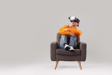 Poster - Emotional young man with virtual reality headset sitting on armchair against light grey background, space for text