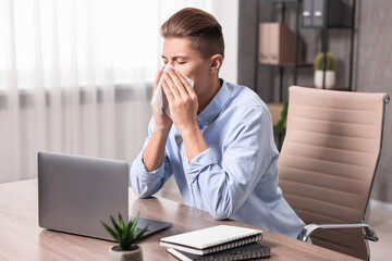 Poster - Young man with tissue suffering from sinusitis at wooden table indoors