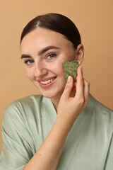 Poster - Beautiful young woman doing facial massage with gua sha tool on beige background