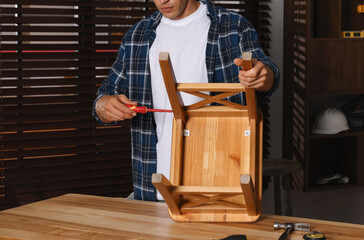 Canvas Print - Man repairing wooden stool with screwdriver indoors, closeup