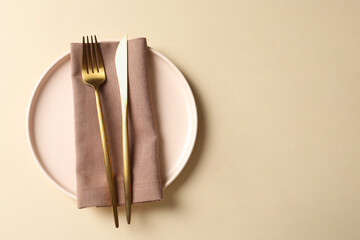 Poster - Stylish golden cutlery, plate and napkin on beige background, top view. Space for text