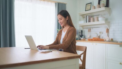 beautiful young asian woman working with laptop computer in home kitchen. work at home