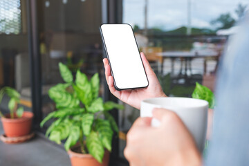 Wall Mural - Mockup image of a woman holding coffee cup and mobile phone with blank white desktop screen