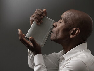 Wall Mural - man praying to god with hands together Caribbean man praying with black grey background with people stock image stock photo	