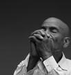 © herlanzer - man praying to god with hands together Caribbean man praying with black grey background with people stock image stock photo