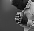 © herlanzer - man praying to god with hands together Caribbean man praying with black grey background with people stock image stock photo