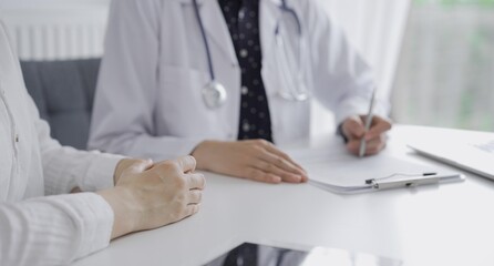 Doctor and a patient. The female physician, wearing a white medical coat over a dark blue dotted blouse, using clipboard and making notes during a consultation in the clinic. Medicine concept