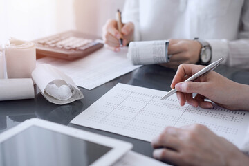 Two accountants use a calculator and tablet computer for counting taxes or revenue balance. Business, audit, and taxes concepts