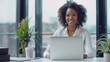 © Ruby Stock - Happy smiling African American businesswoman executive manager sitting at desk working typing on laptop computer in contemporary corporation office with panoramic view. Business technologies concept