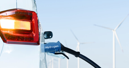 Sticker - Close up of fuel cell car with connected hydrogen fueling nozzle. Wind turbines in the background