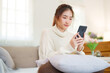 © Pichsakul - Young asian women in sweater enjoying with surfing entertainment on smartphone while sitting on comfortable couch to relaxation and doing activity for spending time with slow life lifestyle at home
